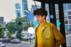 Jovem sorridente de fones nas ruas da cidade, pensando o que colocar no currículo para primeiro emprego sem experiência.