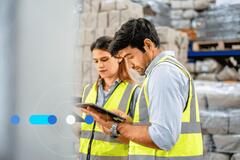 Homem e mulher em armazém de fábrica, vestindo roupas de segurança e pesquisando como e onde contratar profissional de logística.