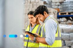 Homem e mulher em armazém de fábrica, vestindo roupas de segurança e pesquisando como e onde contratar profissional de logística.