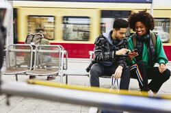 Man and woman looking at phone while sitting on a bench on a train platform.