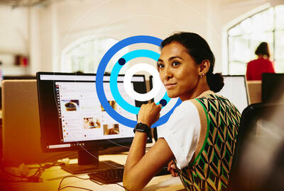 Software de recrutamento Mulher em frente a um computador, sorrindo, com ícones em tons de azul.