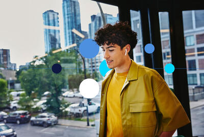 Jovem sorridente de fones nas ruas da cidade, pensando o que colocar no currículo para primeiro emprego sem experiência.