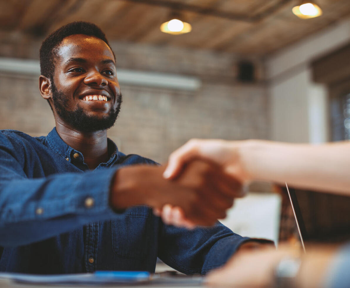 Homem sorridente realizando aperto de mãos com outra pessoa.