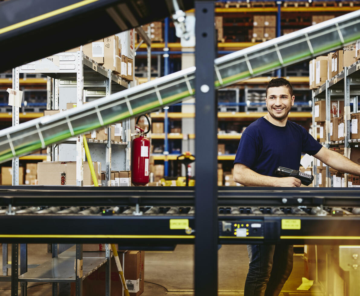 Smiling male standing behind a conveyor belt 
